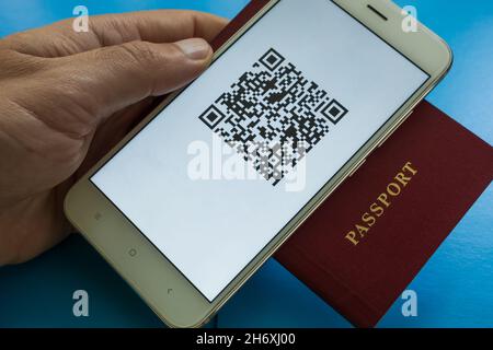 La main d'un homme tient un passeport et un smartphone avec un code QR du certificat de vaccination numérique Covid-19 à l'écran.Gros plan.Arrière-plan bleu Banque D'Images