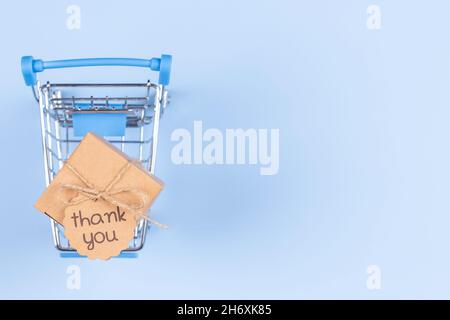 Vue de dessus du mini panier sur fond bleu clair.Boîte en papier Kraft avec inscription étiquette Merci à l'intérieur du chariot.E-commerce, achats en ligne Banque D'Images