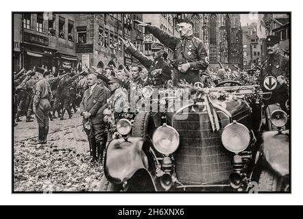 Adolf Hitler en uniforme de sa avec brassard de swastika, debout dans une voiture Mercedes à fleurs et haut ouvert salue le passage des troupes de sa sur un défilé nazi de Nuremberg des années 1930 Julius Streicher célèbre nazi antisémite également présent debout devant un groupe en face d'Adolf Hitler Banque D'Images