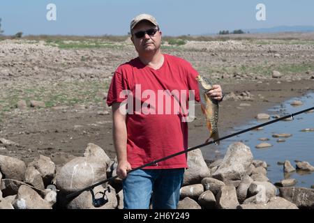 un pêcheur heureux a attrapé un poisson sur une canne à pêche et le tient dans sa main Banque D'Images