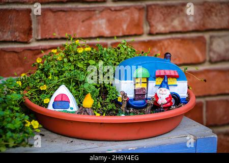 Camping gnome fée jardin en jardinière avec mini campeur et tente contre mur de brique floue. Banque D'Images