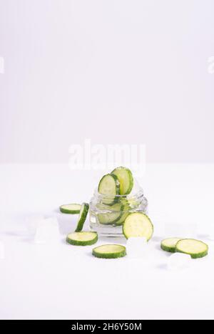 cosmétiques rafraîchissants concombres dans un contenant en verre avec glaçons sur fond blanc. Banque D'Images