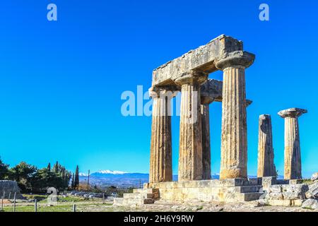 Ruines et colonnes à la Grèce antique de Corinthe sous un ciel extrêmement bleu avec des montagnes enneigées du continent à travers le canal de Corinthe dans la dista Banque D'Images