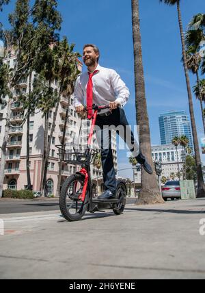 Bon homme d'affaires ont plaisir à monter e-scooter le long de la rue de la ville, e-scouting Banque D'Images