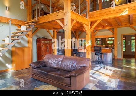 Canapé en cuir Havane dans la salle de séjour avec sol en carreaux gris nuancé, beige et ocre, vue sur la cuisine et la chambre à l'étage à l'intérieur de la maison en bois Banque D'Images