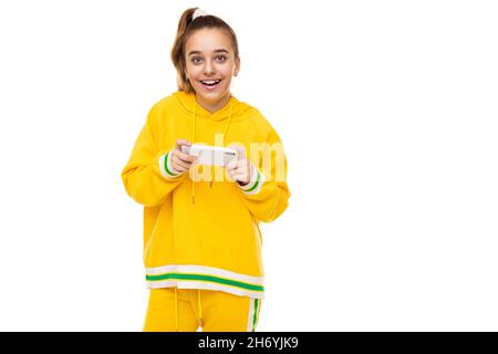 Photo d'une belle surprise souriante gaie mignon fille avec des cheveux foncés avec une queue de cheval dans un élégant jaune tracksuit avec des rayures vertes joue un Banque D'Images