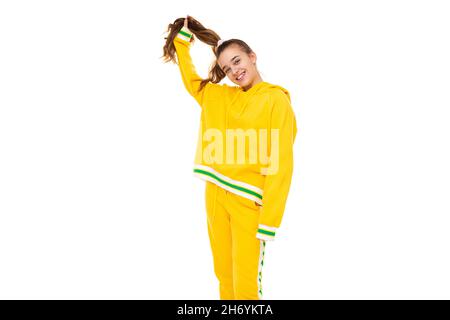 Photo de belle belle fille souriante mignonne avec des cheveux foncés avec queue de cheval dans élégant jaune tracksuit avec des rayures vertes isolées sur blanc Banque D'Images