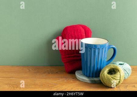 Gants d'hiver, tasse à mug, fil sur table en bois. Fond vert. Espace de copie Banque D'Images