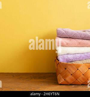 Pile de serviettes de bain dans le panier sur une table en bois. Fond jaune. Espace de copie Banque D'Images