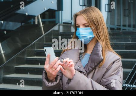 Jeune femme avec masque chirurgical protection du visage utiliser un smartphone tout en marchant à l'extérieur de la ville Banque D'Images