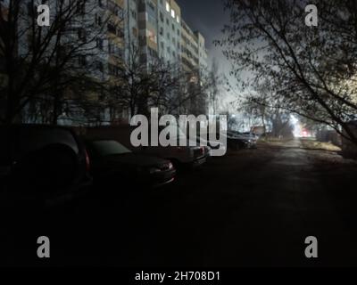 Vue nocturne sombre et défoqué sur la voie et parking près de l'immeuble d'appartements en hauteur en Russie Banque D'Images