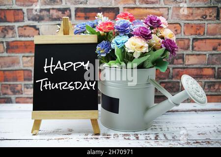 Joyeux jeudi texte sur chevalet en bois noir et vase avec bouquet de fleurs sur fond de mur de brique Banque D'Images