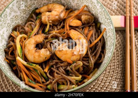 Bol en céramique de délicieux nouilles yakisoba wok aux crevettes sauce brune, servi avec des baguettes, vue d'en haut en gros plan Banque D'Images