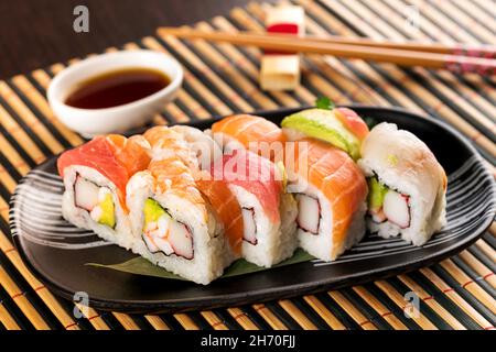 Ensemble de petits pains à sushis arc-en-ciel uramaki avec thon, saumon et avocat, servi au restaurant sur un tapis de bambou Banque D'Images