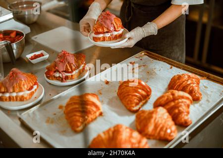 Le confiseur en gants tient une assiette avec un délicieux croissant dans une boulangerie artisanale Banque D'Images