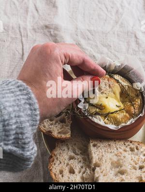 Trempez à la main un morceau de pain au levain dans un plat de fondue au fromage camembert. Banque D'Images