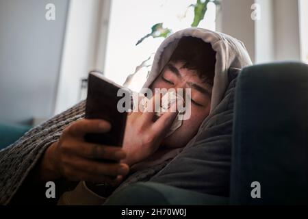 Homme malade sur le canapé à l'aide d'un téléphone cellulaire Banque D'Images