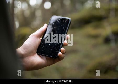 Main tenant un smartphone mouillé dans la forêt Banque D'Images