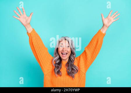 Portrait d'une femme aux cheveux gris émerveillés et attirante qui se lève les mains vers le haut, se réjouissant d'être isolée sur fond turquoise clair de couleur sarcelle Banque D'Images