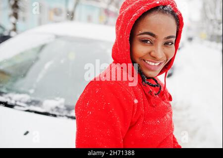 Femme afro-américaine à capuchon rouge voiture propre de la neige en hiver. Banque D'Images