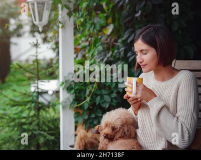 Jeune femme asiatique se reposant à l'extérieur avec une tasse de café sur le porche de la maison de campagne, se glaçant à l'extérieur avec le chien de poule . style de vie d'automne, temps libre de loisirs concept.Copier l'espace Banque D'Images