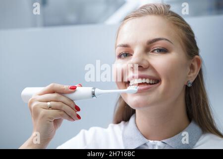 Gros plan d'une charmante jeune femme dentiste souriant, utilisant une brosse à dents électrique sur ses dents Banque D'Images