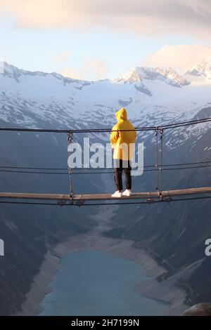 L'homme est seul avec une veste de pluie jaune sur un pont suspendu.Olperer Banque D'Images