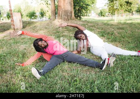 Deux filles afro-américaines sont engagées dans le sport, faisant des exercices assis dans le parc sur l'herbe. Banque D'Images