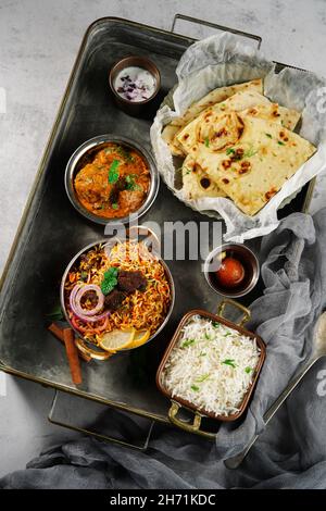 Repas indien thali - Mutton biryani, raita, kafta malai, riz basmati, naan de beurre et jamun gulab servi sur un plateau Banque D'Images
