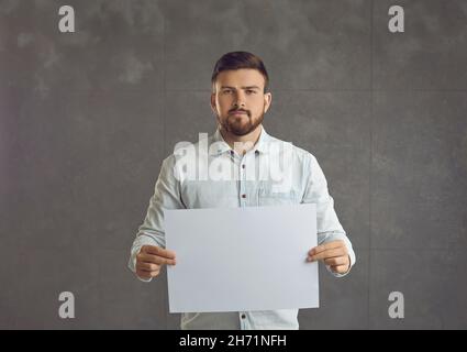 Jeune homme, avec une barbe, tenant une feuille de papier vierge, sérieux. Banque D'Images