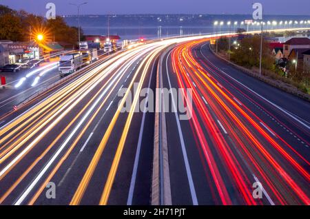 Autoroute de banlieue en soirée.Traces des phares et des feux arrière de circulation intense et des feux sur le pont Banque D'Images