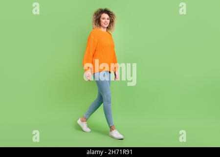 Photo pleine grandeur de belle blonde curly coiffure dame aller porter chandail orange jeans chaussures isolées sur fond vert Banque D'Images