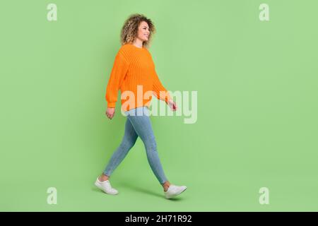 Pleine taille photo de profil de belle blonde dame Go porter orange pull jeans baskets isolées sur fond vert Banque D'Images