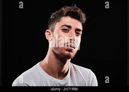 Jeune homme gros plan portrait sur fond noir.Il porte une chemise blanche de base et regarde l'appareil photo. Banque D'Images