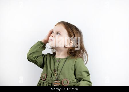 Une petite fille d'avant-chooler aux cheveux rouges sur un fond blanc regarde soigneusement vers le haut.Studio photo de penser enfant Banque D'Images