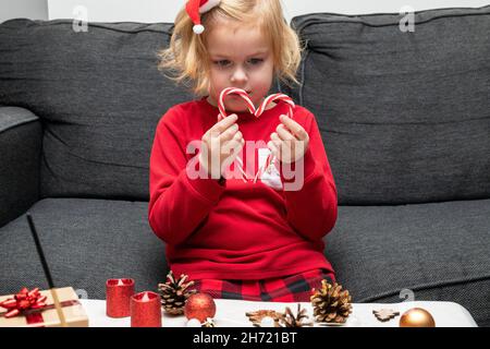 Petite fille portant un pyjama de noël, faisant de l'artisanat et jouant avec des cannes de bonbons.Décoration d'arbre de Noël à faire soi-même. Banque D'Images