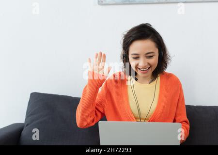 un jeune opérateur heureux dans un micro-casque agitant la main pendant un appel vidéo Banque D'Images