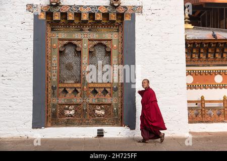 Un moine bouddhiste passe devant une fenêtre de travail en treillis dans un dochey ou une cour dans le Punakha Dzong à Punakha, au Bhoutan. Banque D'Images