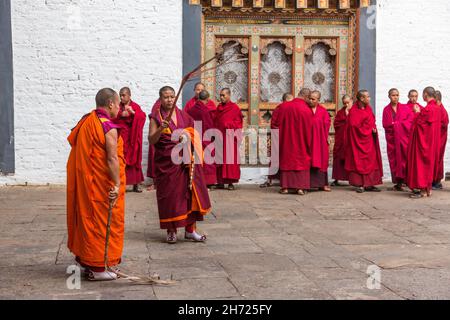 Un groupe de moines bouddhistes dans une cour du Punakha Dzong à Punakha, au Bhoutan.Deux moines portent des fouets en cuir. Banque D'Images