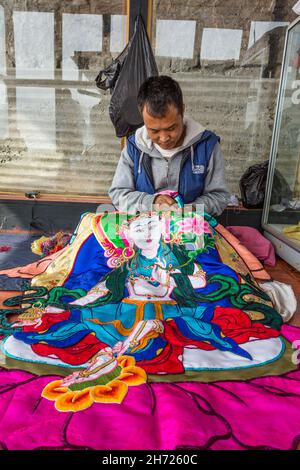 Un homme bhoutanais fait une applique en soie thangka ou un mur religieux bouddhiste suspendu représentant Budda.Dochu la, Bhoutan. Banque D'Images