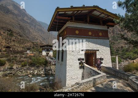 Un homme bhoutanais dans le gho traditionnel devant une chaîne de fer qui se promeusse sur la rivière Paro par le temple de Tamchhog Lhakhang.Paro, Bhoutan. Banque D'Images