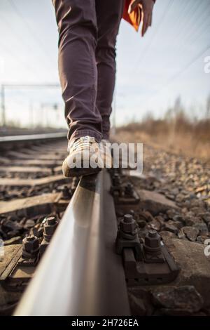 Les pieds mâles en bottes jaunes marchent en toute confiance le long des voies ferrées, sur un fond flou.Marche dangereuse. Banque D'Images