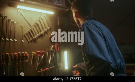 Déterminé jeune forgeron dans des combinaisons bleues vérifiant ses outils et fournitures pour se rendre au travail dans son atelier Banque D'Images