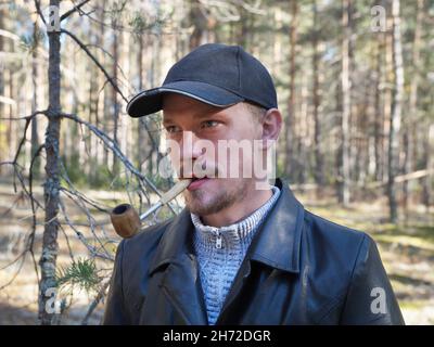 portrait d'un jeune homme avec une pipe à fumer dans la bouche dans la forêt. Banque D'Images