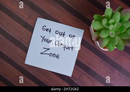 Sortez de votre zone de confort écrire sur les notes adhésives isolées sur la table en bois. Banque D'Images