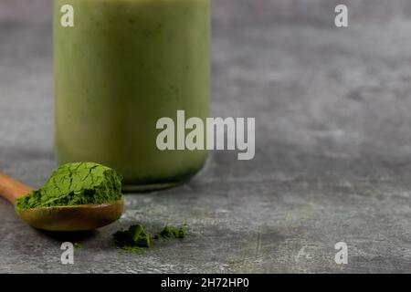 Un gros plan d'une cuillère de poudre de thé vert matcha avec un latte matcha derrière Banque D'Images