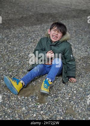 brunette enfant assis au sol pleure inconsolable avec les yeux fermés en hiver à l'extérieur avec une parka. verticale. concept de frustration dans le chi Banque D'Images