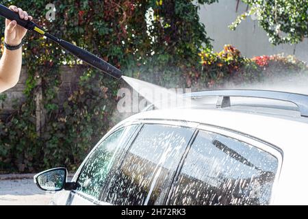 Un homme lave sa voiture dans un lave-auto. Un homme lave une voiture dans un lave-auto manuel.Dégager la voiture Banque D'Images
