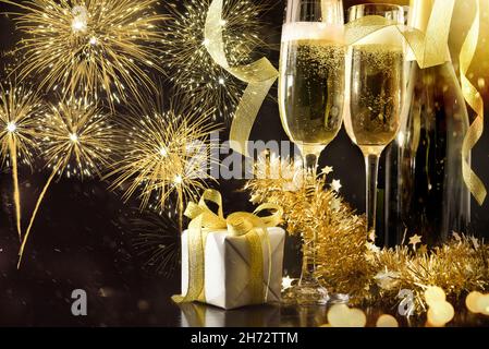 Fête de la Saint-Sylvestre avec verres à vin pétillant et bouteille décorés de rubans cadeaux et de décorations dorées sur table noire Banque D'Images