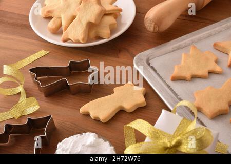 Table en bois avec des biscuits aux formes de Noël fraîchement cuites sur un plateau de cuisson et une assiette avec des moules.Vue en hauteur.Composition horizontale. Banque D'Images